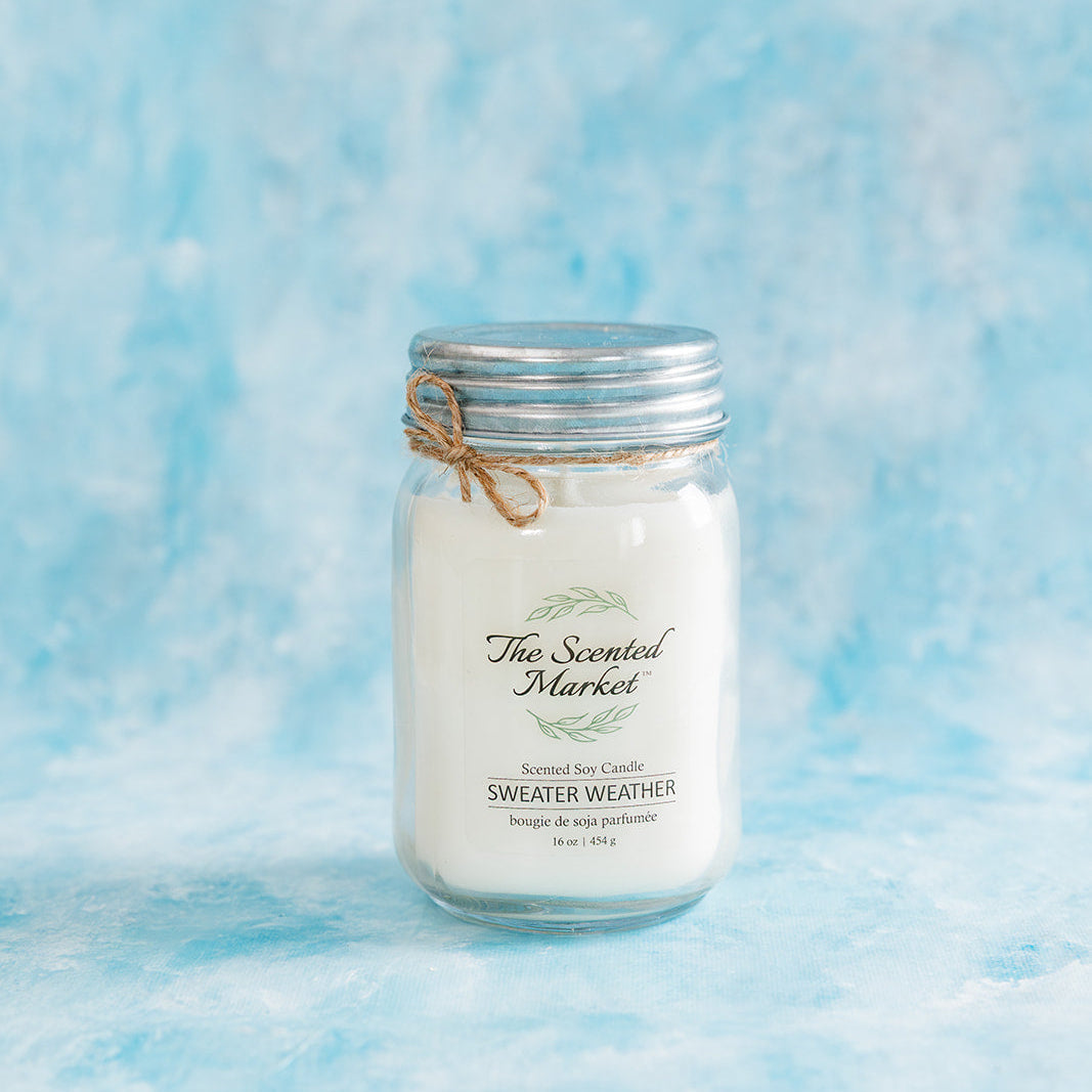 Candle in a mason jar with 'The Scented Market' label on a blue textured background