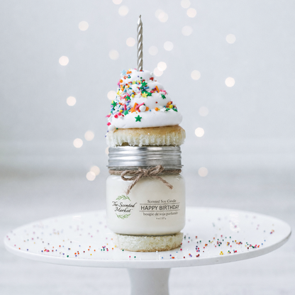 Decorative candle with a small cake on top and sprinkles, featuring 'The Scented Market' branding.