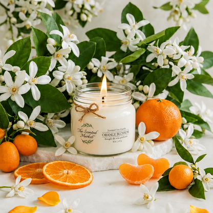 Candle with orange fragrance surrounded by flowers, oranges, and orange slices on a light background